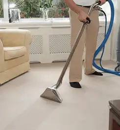 Professional carpet cleaner using a hot-water extraction wand and hose machine in a living room in Orange, CA.