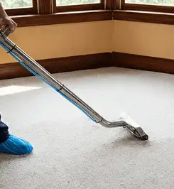 Steam carpet cleaning technician using a hot-water extraction wand on a residential carpet, wearing blue protective shoe covers Orange, CA.