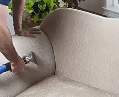 Professional upholstery cleaner deep-cleaning a fabric sofa with a handheld extraction tool and hose in Orange, CA.